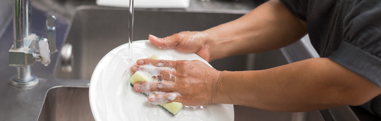 Woman hands washing white plate in kitchen sink